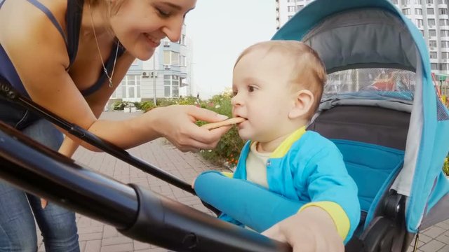 Young mother giving cookie to her baby son sitting in pram