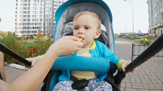 Portrait of 1 year old baby boy sitting in pram and eating biscuit