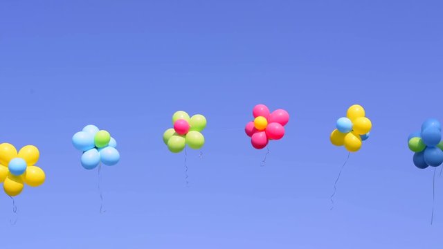 A sting of colorful, helium filled balloons with decorative ribbons rise in an arch against a vibrant blue sky..