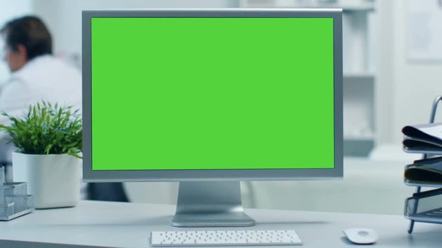 Close-up of a Monitor with Green Screen. Doctor Working at his Desk in the Background. Shot in a Modern Medical Office. Shot on RED Cinema Camera 4K (UHD).