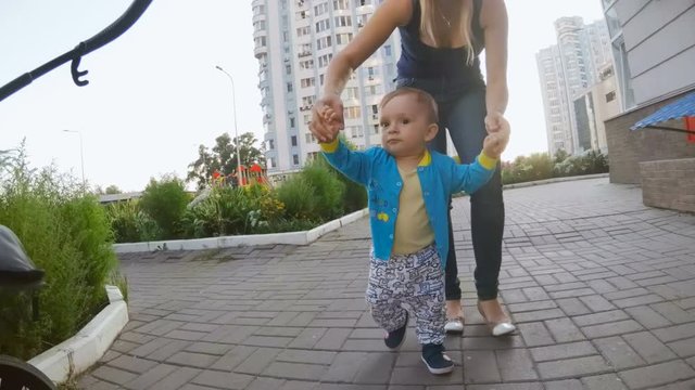 Young mother holding her baby by hands and walking at street