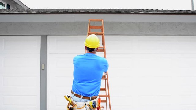 A contractor wearing a tool belt climbs a ladder and conducts a quick roof assessment on a residential home..