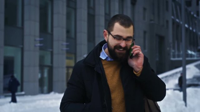 Man walking smiling and talking on phone on business street, conversation near office building hd