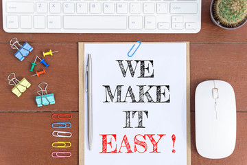 Text We make it easy on white paper which has keyboard mouse pen and office equipment on wood background / business concept.