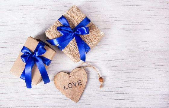 Two gift boxes with blue ribbons and a heart from a tree on a white wooden background. Valentine's day. Copy space.