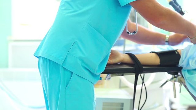 Anesthesiologist preparing patient for cosmetic surgery on breasts in hospital operating room. Blood pressure cuff on arm of patient under anesthesia. Breast augmentation enlargement. Mammaplasty.