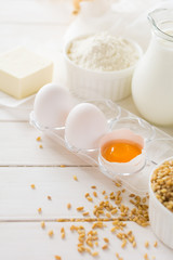 Ingredients for baking: flour, milk, wheat grain, butter and eggs on white wooden background. Selective focus
