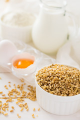 Ingredients for baking: flour, milk, wheat grain, butter and eggs on white wooden background. Selective focus
