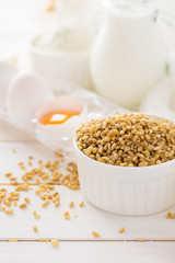 Ingredients for baking: flour, milk, wheat grain, butter and eggs on white wooden background. Selective focus
