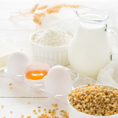 Ingredients for baking: flour, milk, wheat grain, butter and eggs on white wooden background. Selective focus
