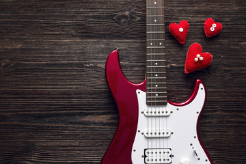 Red electric guitar with hearts on a dark wooden background. Spa