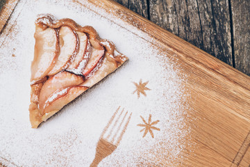 A piece of sliced apple pie with cinnamon on vintage wooden background texture. Top view.