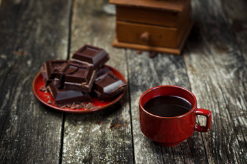 Coffee red cup, pieces of chocolate on wooden table background. Tinted. Selective focus.