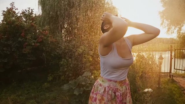 Slow motion footage of laughing young woman dancing under summer rain at sunset