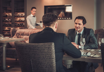 Two confident business men have business lunch at restaurant