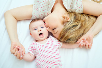 Mother kisses baby lying on the bed closeup.