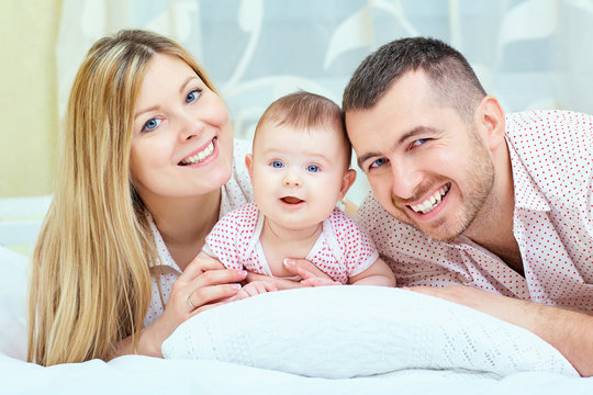 Beautiful mother, father and baby lying on the bed. Happy family, parents and a small child.