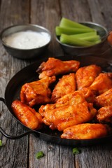 Homemade spicy Buffalo chicken wings served with blue cheese dip celery sticks and baby carrots on rustic wooden background