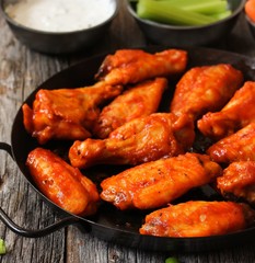 Homemade spicy Buffalo chicken wings served with blue cheese dip celery sticks and baby carrots on rustic wooden background