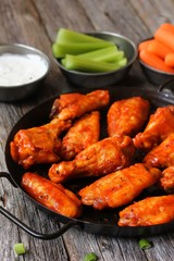 Homemade spicy Buffalo chicken wings served with blue cheese dip celery sticks and baby carrots on rustic wooden background