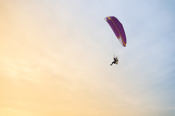 Naklejka na ściany i meble Paraglider against on blue and yellow sky (parachute, paragliding)