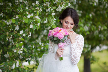 Young bride with wedding bouquet in blooming garden