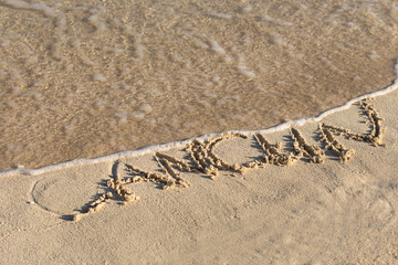 Inscription Cancun on sandy beach with wave's foam