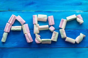 ABC letters made of marshmallow candies, view from above, isolated, blue wooden background