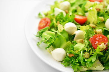 Fresh salad on a white plate on white table in restaurant.