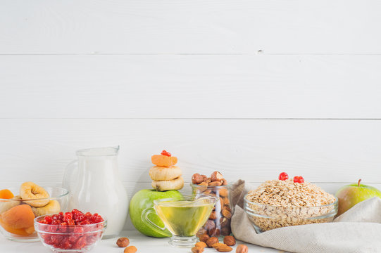 Ingredients for healthy breakfast on white wooden background, copy space. Fresh and dried fruit, nuts, oatmeal, honey and yogurt. The concept of natural organic food, diet. 