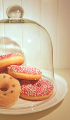 Clopseup assorted donuts on a plate covered glass bell. White painted wooden planks on background. Warm light