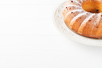 Bundt cake with cottage cheese, raisins and sugar powder on a white plate with copy space. Homemade ring cake with icing sugar on white wooden table, closeup. Sweet food.