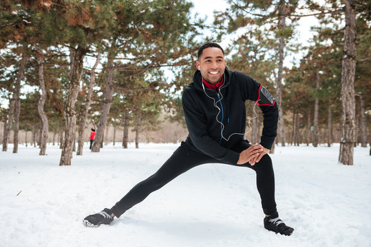 Young Fitness Man Stretching Leg Muscles Outdoors In Winter Forest