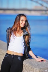 Portrait of cute young girl smiling brunette leaning on the stone edge of the embankment on blurred...