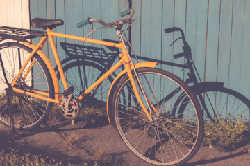 Naklejka na ściany i meble Yellow old vintage bicycle leaning against on vintage wood wall background in the sun. Bicycle vintage for decorate concept.