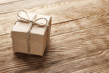 Gift box in kraft paper with bow on wooden background