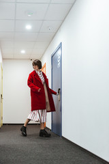 Woman in red coat walking at corridor and opening door