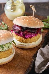 Two vegetarian hamburgers with onion and cheese cutlets, avocado salad, arugula, fried beetroot and yogurt sauce on wooden serving board over texture background. Healthy fast food.