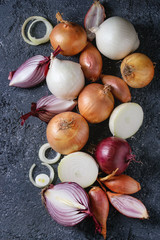 Variety of whole and sliced red, white, yellow and shallot onions over dark stone texture background. Top view, space for text © Natasha Breen