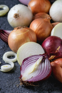Variety of whole and sliced red, white, yellow and shallot onions over dark stone texture background. Close up, space for text
