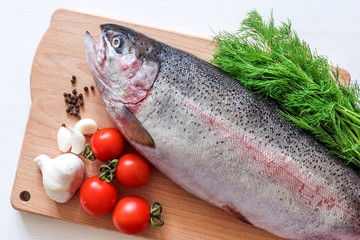 raw rainbow trout on a cutting board with vegetables and spices