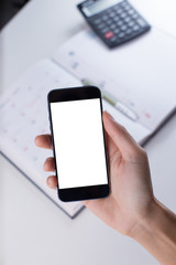 A female hand holding smart phone with office stationeries at working desk