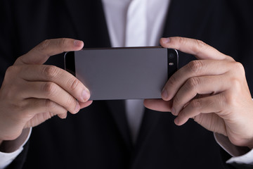 A man in black casual suit holding his mobile phone taking photo