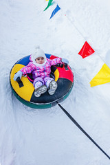 Toddler girl sitting in inflatable sledge (snow tube), waiting for a sliding fun.