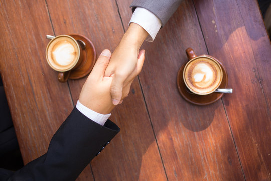 Business talk and hands shake at a coffee shop with two cups of latte