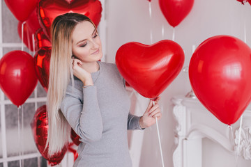 Beautiful young woman posing with red heart balloons in a white room. Valentine's Day