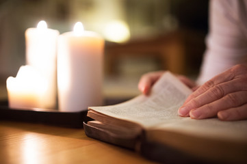 Unrecognizable woman reading Bible. Burning candles next to her.