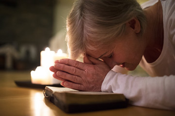 Senior woman praying, hands clasped together on her Bible.