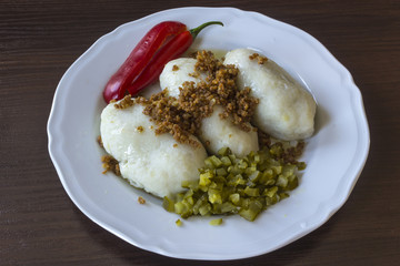 Potato dumplings - a traditional regional dish. Polish and Lithuanian cuisine. With pickles , fried bacon and paprika on a white plate on a dark background ..