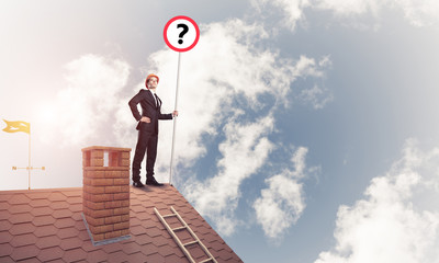 Businessman on brick house roof showing banner with question mar